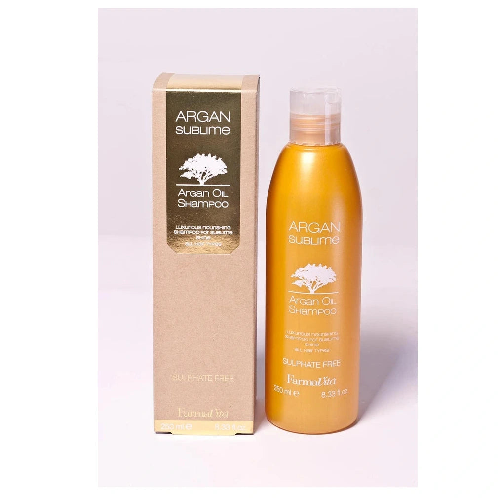 Argan Sublime Argan Oil Shampoo bottle in a metallic gold finish next to its brown kraft paper packaging box, on a light lavender background.